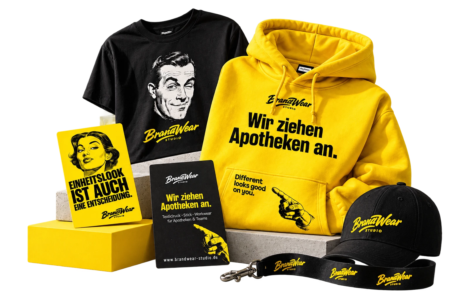 Freigestelltes Ensemble von BrandWear Studio: gelber Hoodie mit dem Claim „Wir ziehen Apotheken an.“, schwarzes Shirt mit zwinkerndem Retro-Mann, beidseitig bedruckte Visitenkarten auf Steinpodesten, schwarze Cap und Lanyard mit Logo.